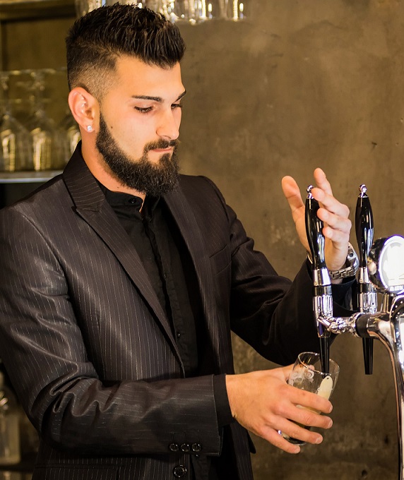 a neatly dressed man operating a beer tap.